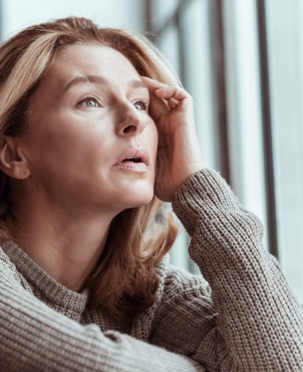 Near window sill. Beautiful pleasant mature woman wearing sweater standing near the window sill