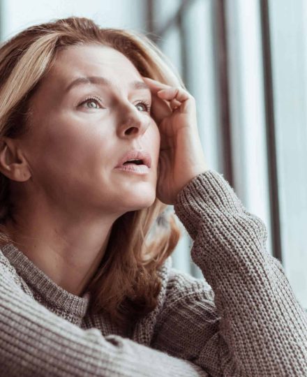 Near window sill. Beautiful pleasant mature woman wearing sweater standing near the window sill